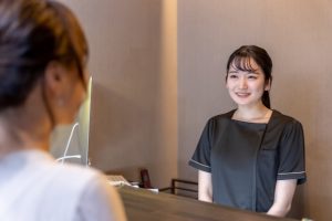 美容院の受付スタッフが笑顔でお客様に対応している写真。予約確認や接客の雰囲気が伝わる。