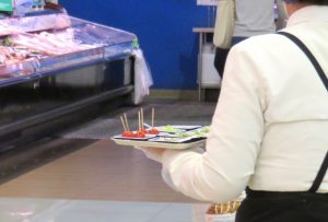 スーパーで試食を配布するスタッフの背中とトレーの様子