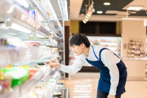 スーパーで棚の商品を手前に並べてフェイスアップするスタッフ｜Fronting products on shelves at a supermarket
