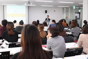 大きな会場で行われる添乗員の説明会で講師の話を聞く参加者