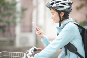 自転車に乗りながらスマホで配布範囲を確認する店舗PRスタッフ