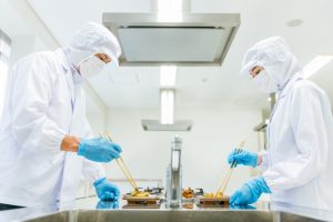 白衣姿で惣菜の盛り付け作業を行う食品工場スタッフ