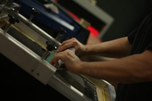 印刷会社の現場で機械のそばに立ち手元作業をしている様子