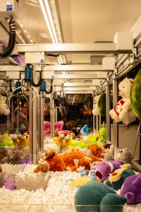 クレーンゲーム機が並ぶゲームセンター店内と、景品補充や巡回作業をイメージした写真